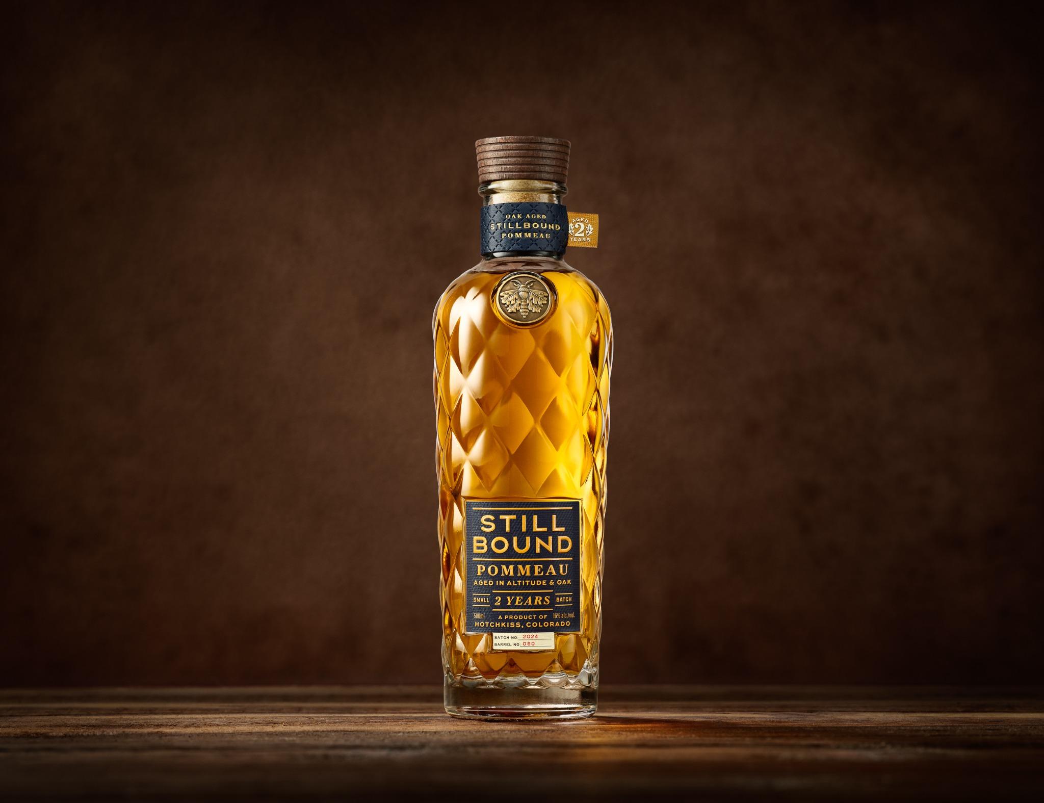 Stillbound Pommeau, glowing amber through diamond glass, photographed on a wooden surface